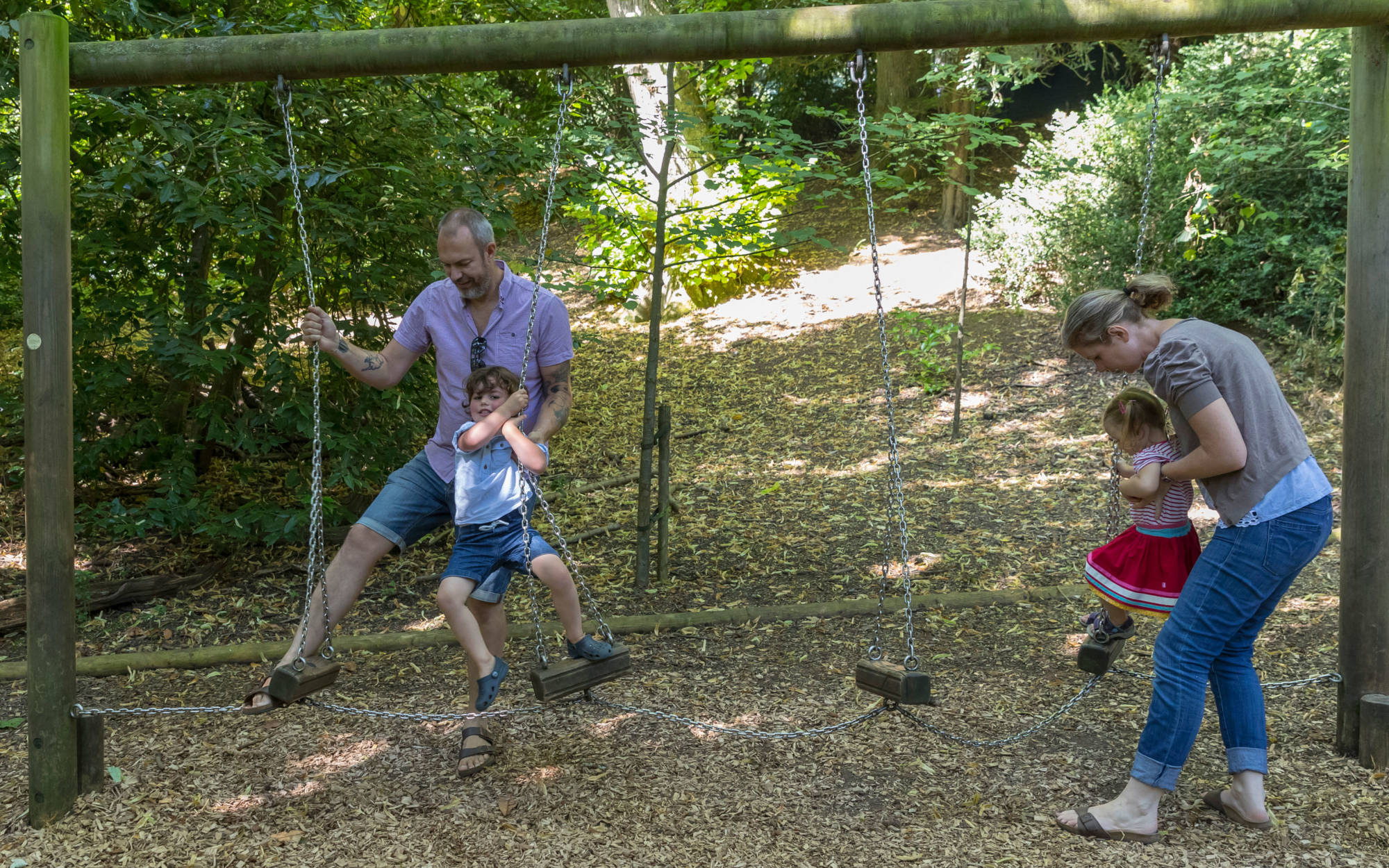 Famiy with children playing on the swings in the Woodland Playground