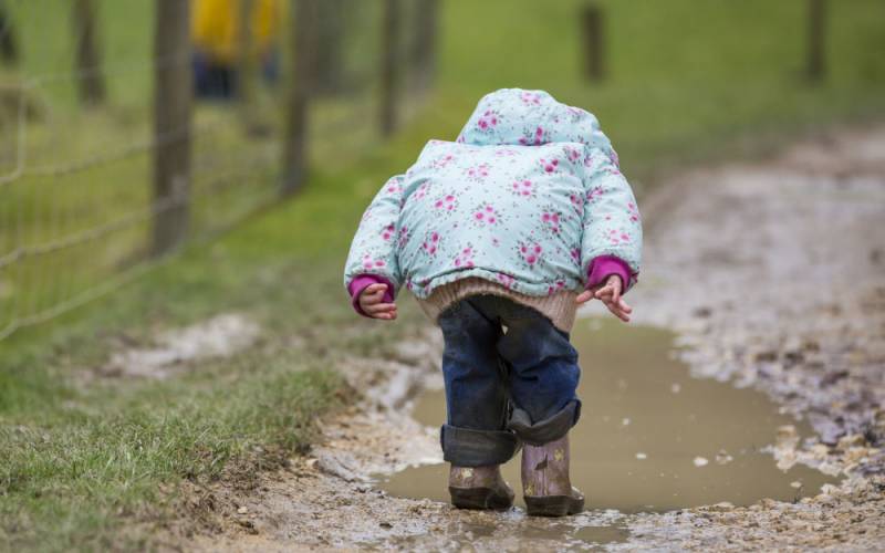 Little girl wearing wellies splashing in muddy puddles